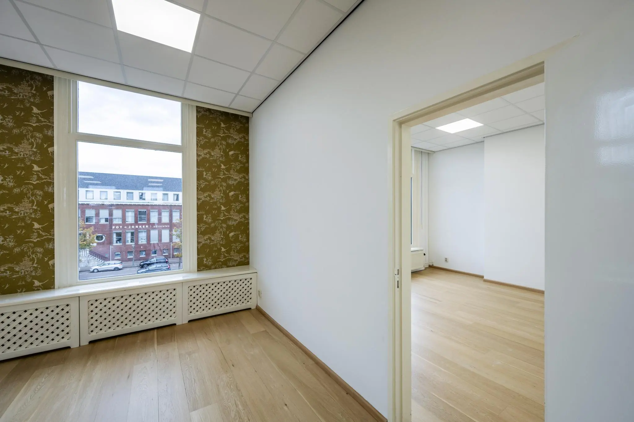 Lichte kantoorruimte aan de Nieuwe Gracht met houten vloer, systeemplafond en uitzicht op een bakstenen pand.